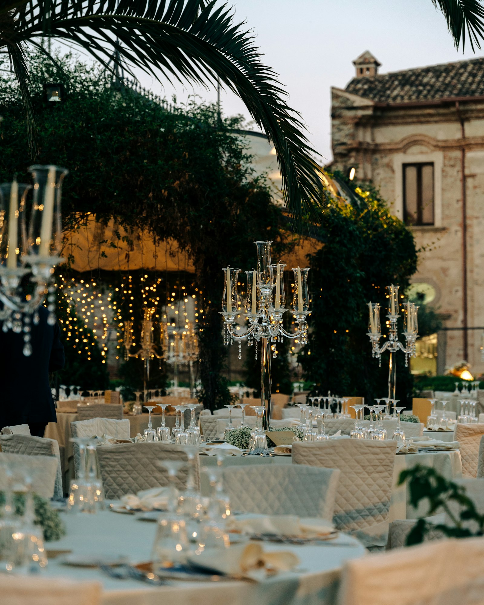 An elegant candlelit wedding reception at dusk with candelabra, glassware and string lights