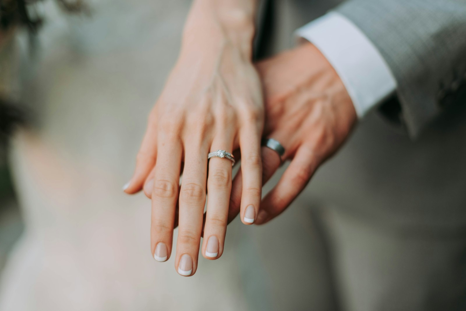 A couple's hands resting together, wedding and engagement rings in soft focus
